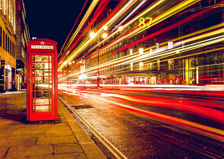 time-lapse photo of vehicle creating light streaks near telephone booth