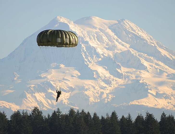 man using green parachute during daytime and mountain alps at distance