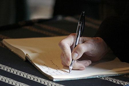 person holding ballpoint pen writing on white paper