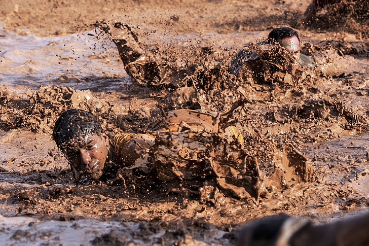 men crawling on mud during daytime