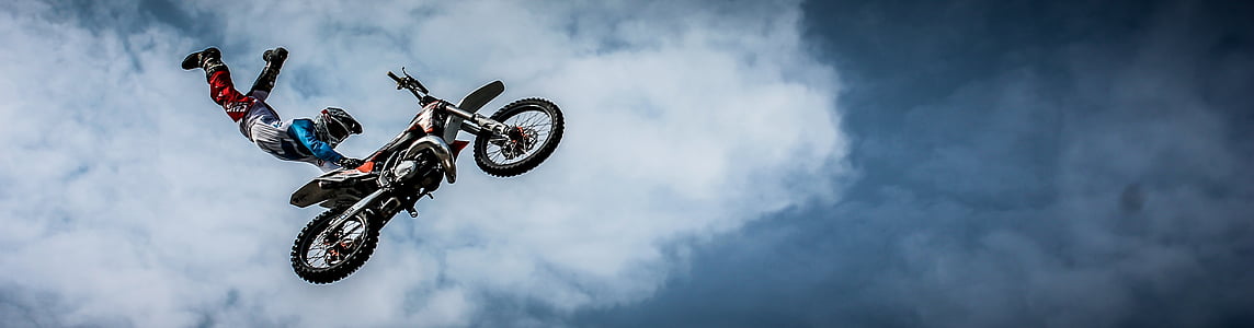 sports photography of motocross racer holding motocross dirt bike seat while suspended on air
