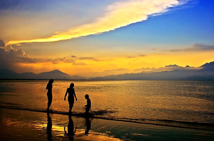 silhouette of three person walking on beach shore during sunset