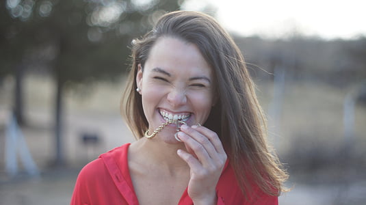 woman wearing red top biting gold necklace during daytime