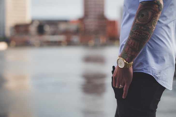 selective focus photography of man in white shirt, gold-colored analog watch, and black bottoms