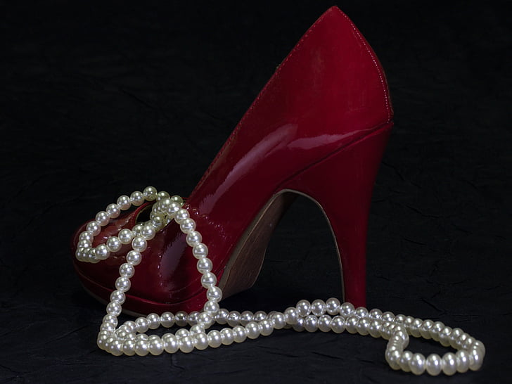 unpaired women's red leather stiletto with white pearl necklace