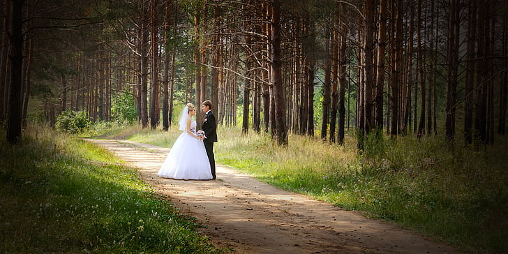 man and woman wearing wedding dress standing on road between trees