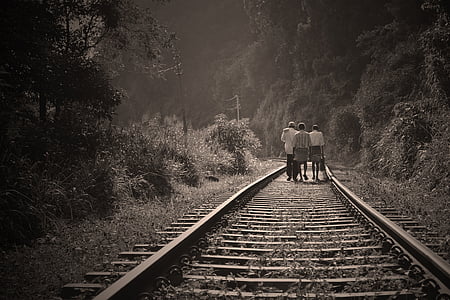 grayscale photo of three persons walking on railway