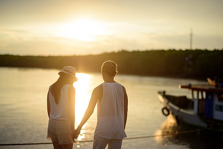 man and woman holding hand beside body of water during daytime