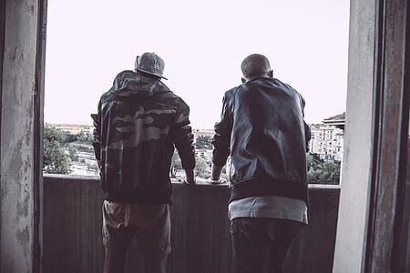 two men wearing jackets standing on balcony