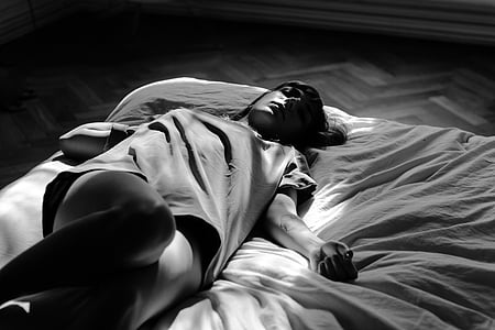 grayscale photography of a woman wearing t-shirt laying on bed
