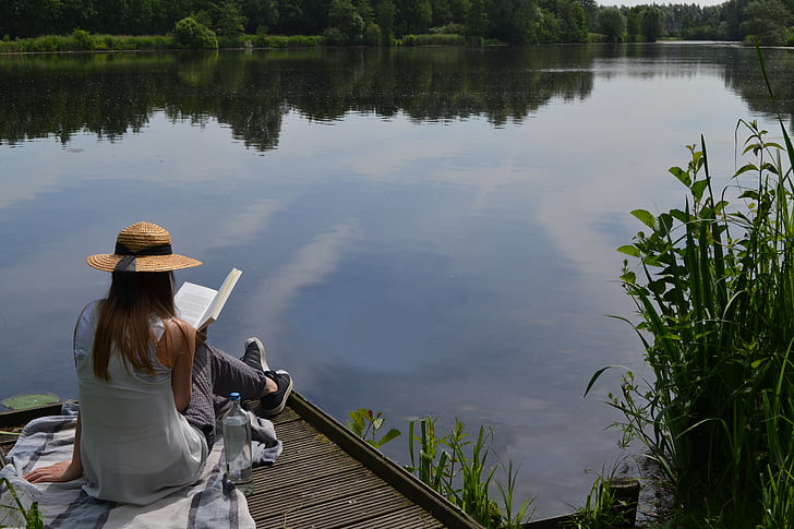 woman in gray sleeveless top reading book beside sitting on dock during daytime