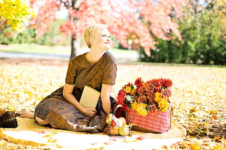 woman wearing brown floral dress sitting beside basket of red and yellow petaled flowers