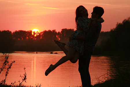 silhouette of man carrying a girl in front of water pond during sunset