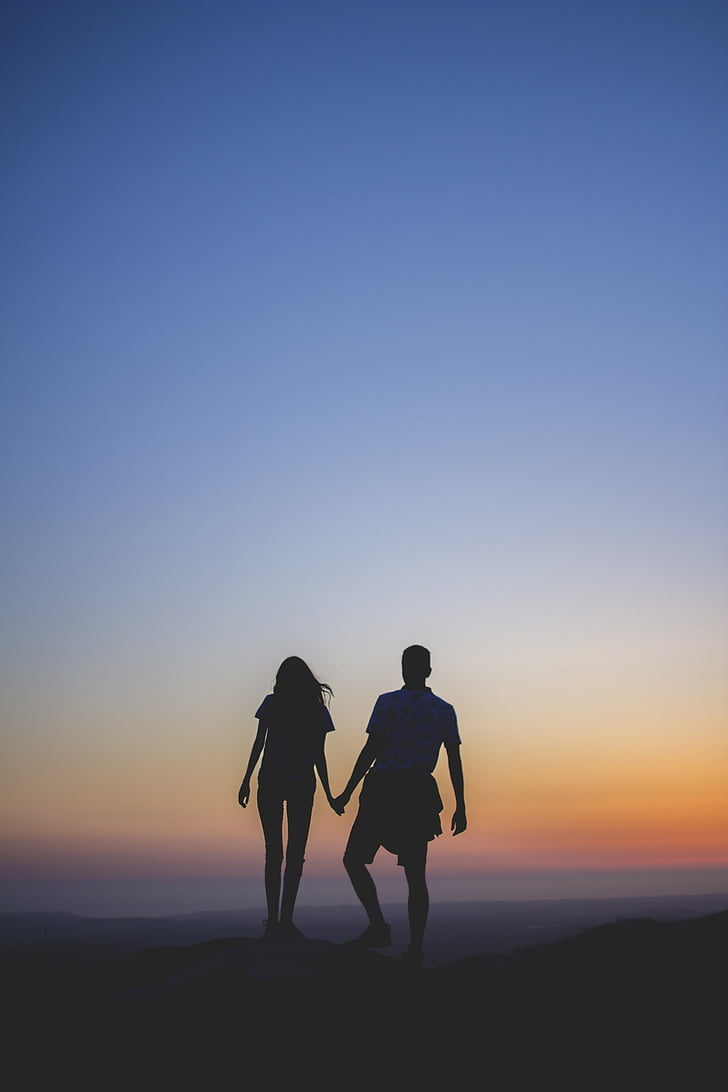 silhouette of couple on mountain edge during sunset