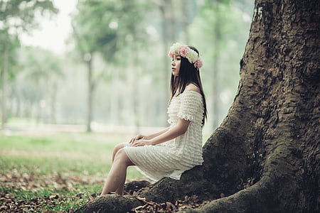 woman in white off-shoulder dress sitting near tree