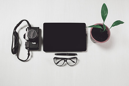 black tablet computer near camera, potted plant, twist pen, and black-framed eyeglasses