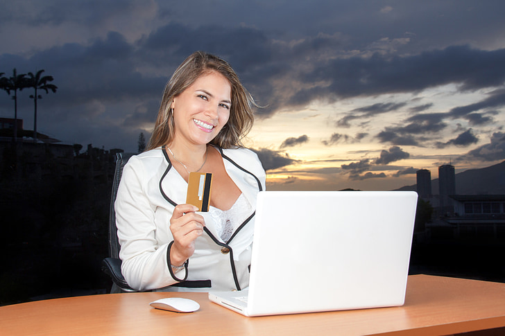 woman wearing white blazer holding a brown and black labeled magstripe card in front of white laptop computer