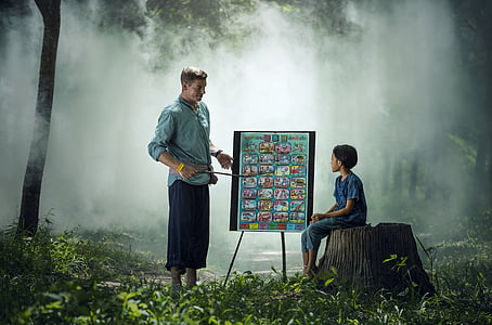 person holding a stick pointing an Alphabet chart and child sitting looking on the chart