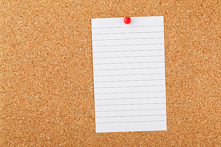 white page of notepad and brown cork board