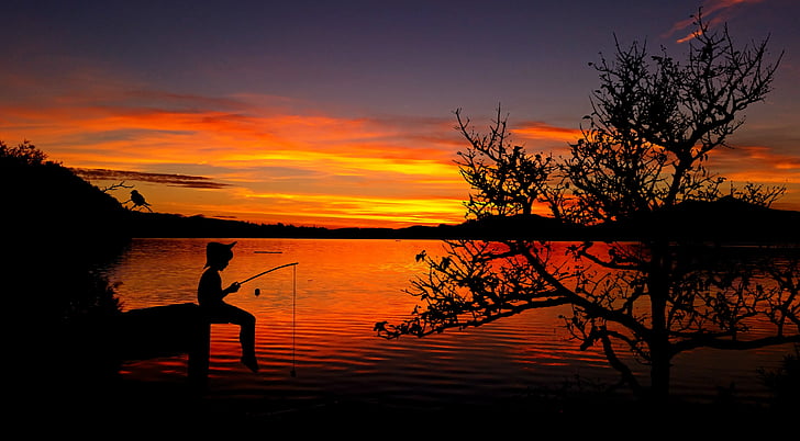 silhouette of boy fishing on dock