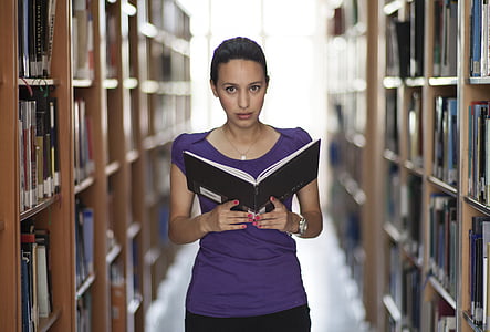 woman in purple top holding book in library