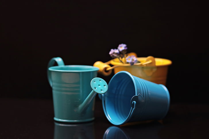 green watering can beside blue and yellow buckets