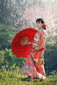 woman wears pink and multicolored floral dress holds red folding umbrella