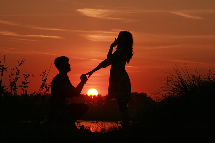 silhouette of man holding ring to woman