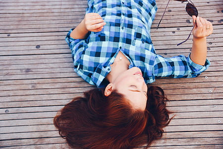 woman wearing blue and white plaid shirt lying on brown wooden pavement