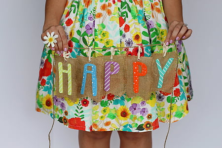 person wearing yellow and red floral dress holding happy text printed hanging decor