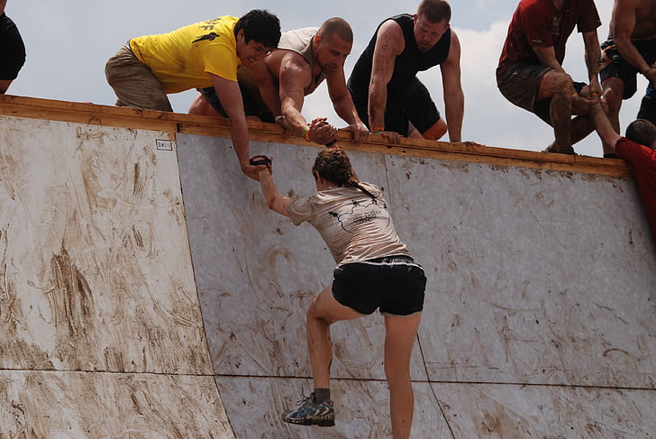 woman climbing on wall and two man helping