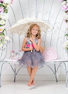 smiling girl in gray sleeveless dress sitting on white bench holding white umbrella