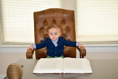 boy sitting on office chain in front of book