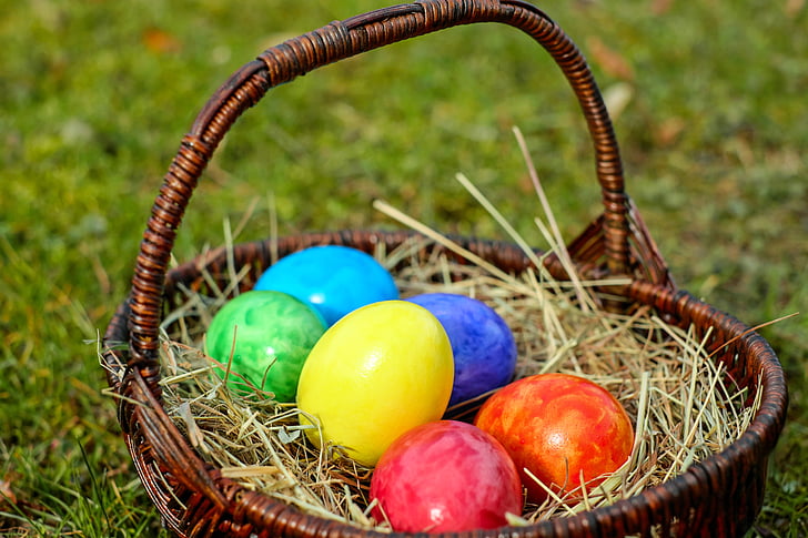 assorted-color Easter eggs in brown wicker basket on green grass