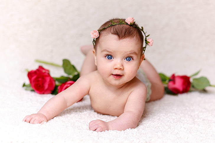 focus photography of baby near red roses