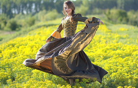 woman wearing yellow and gray dress standing on the middle of yellow field of flowers