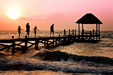 photography of silhoutte of four persons walking on sea dock