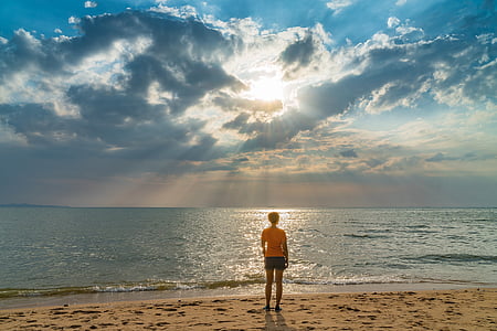 photo of person standing seashore facing ocean during day time