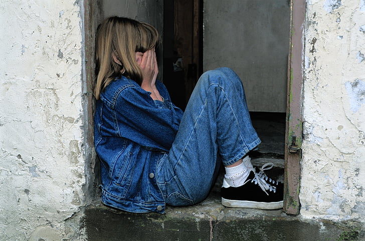 girl in blue jeans and denim jacket with black sneakers covering her face