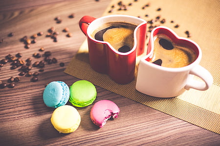 two white and red heart-shaped ceramic mugs with multicolored French macaroons