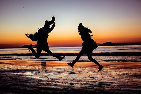 silhouette photo of two person jumping beside body of water