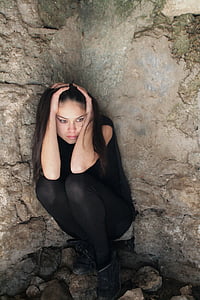 woman in black pants crouching near rocks