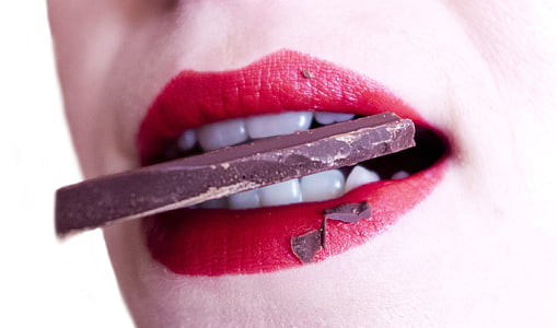 woman with red lipstick biting black chocolate