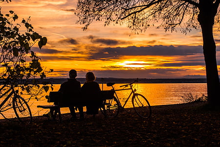 silhouette of couple sitting on bench near body of water during golden hour