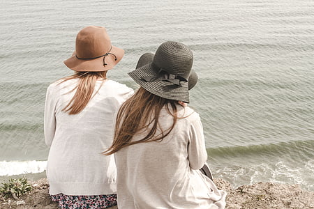 two women near water wearing hat and white top
