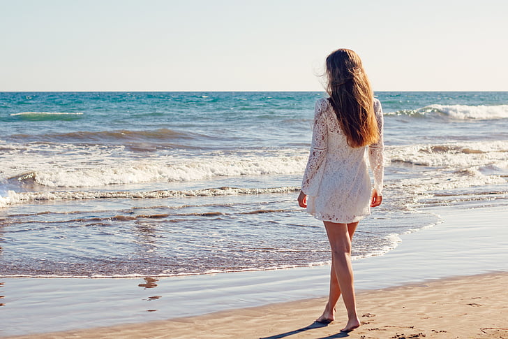 woman in white lace long-sleeved dress stands beside seashore
