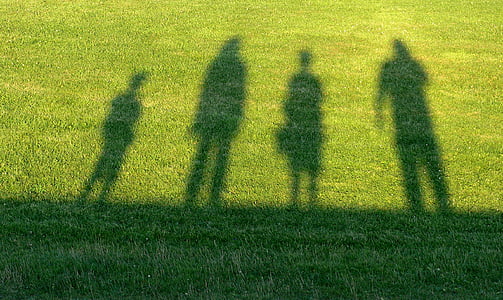 four person shadow on green grass field
