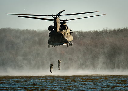 two soldiers hanging under brown helicopter during daytime
