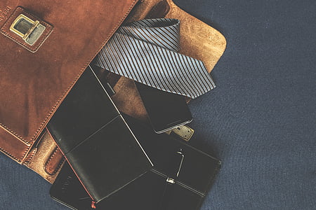 close up photo of bag filled with gray necktie long wallet and book
