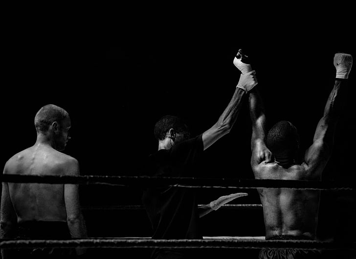 referee raising up boxer's hand while the other boxer is standing behind